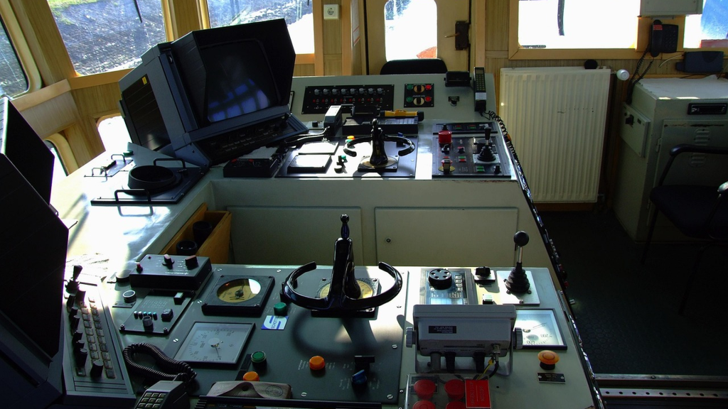 Real ship's bridge command center with marine computer console, navigation controls, helm wheel, and instrument panels