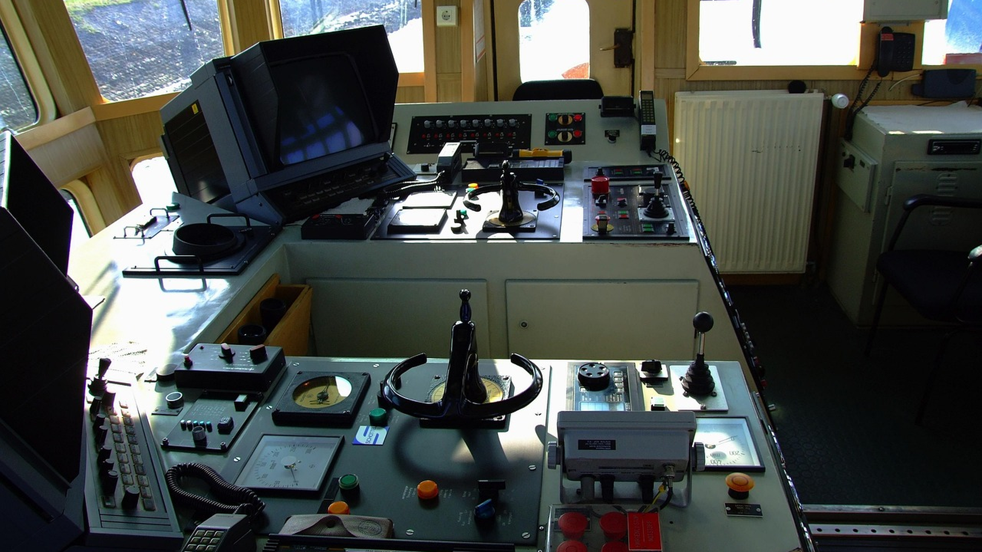 Real ship's bridge command center with marine computer console, navigation controls, helm wheel, and instrument panels