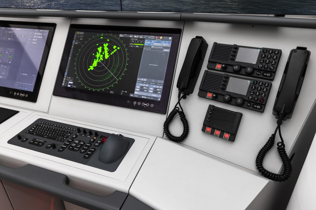 Close-up of a marine bridge LCD display panel mounted in a brushed-steel console with a navigation chart faintly visible on screen