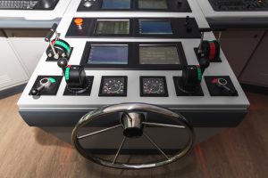 Vehicle And Heavy Equipment image by Seatronx Modern commercial ship bridge console with a stainless steel steering wheel, throttle controls, instrument gauges, and a row of flush-mount marine navigation displays at the helm.
