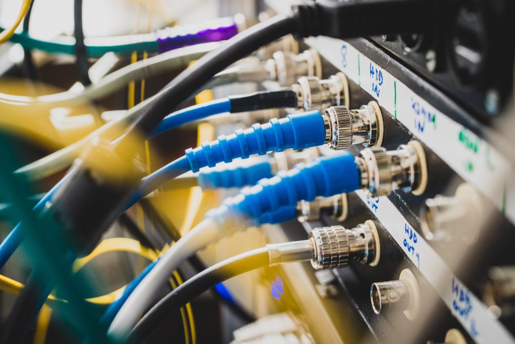 Blue BNC SDI signal cables plugged into the back of a 1U patch panel from above -- the broadcast-grade interconnect that still anchors the back panel of a commercial marine bridge display.