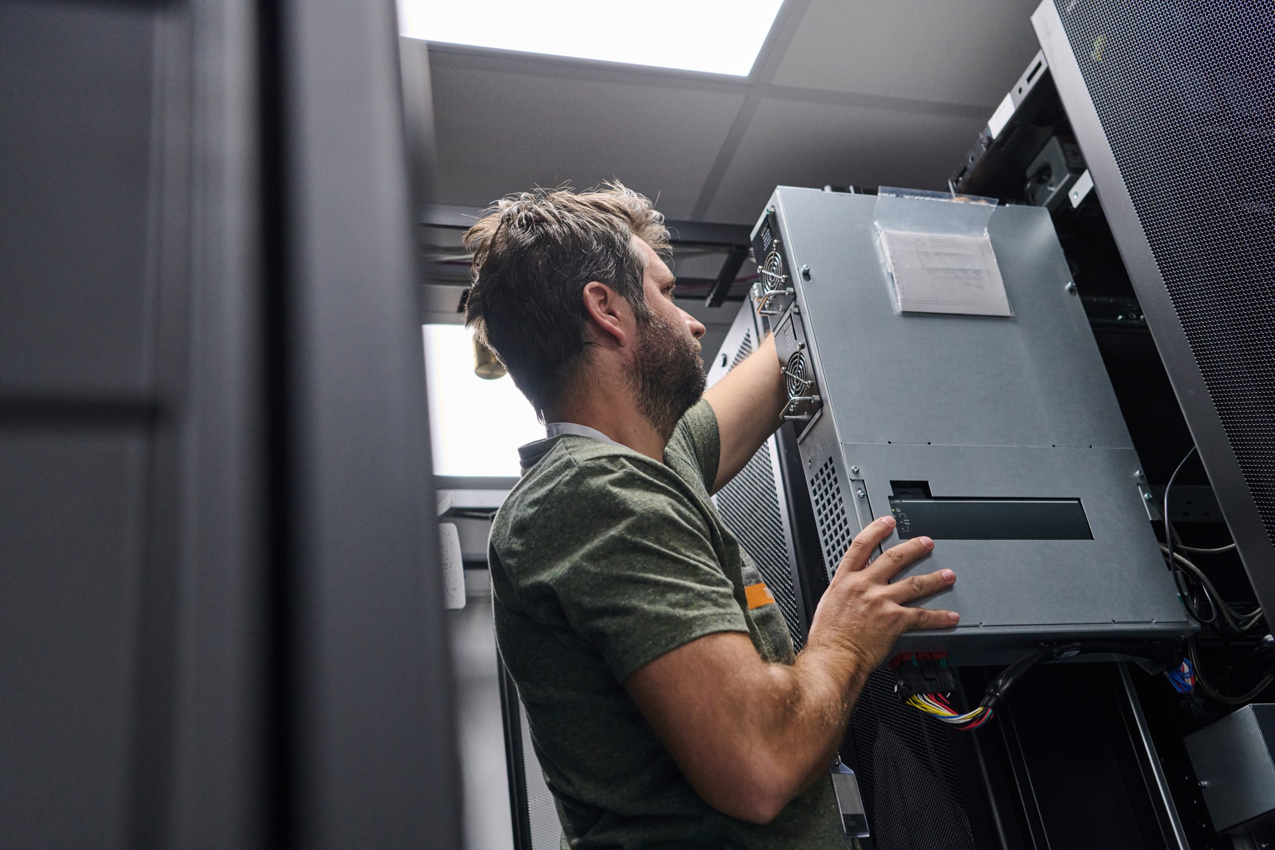 IT technician installing a rugged server chassis into a marine equipment-room rack cabinet