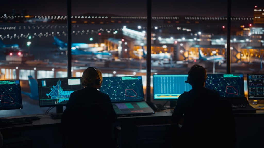 Air traffic controllers at a darkened radar console showing static range rings, an airspace map, and target data blocks on continuous-duty displays, illustrating the burn-in resistance, low-light readability, and round-the-clock reliability an air traffic control display must have.