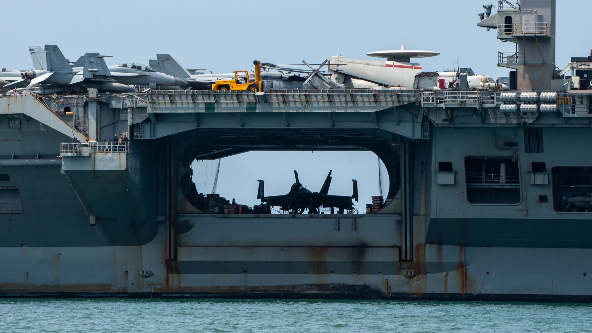 Aircraft carrier with aircraft on deck and a jet silhouetted inside an open bay