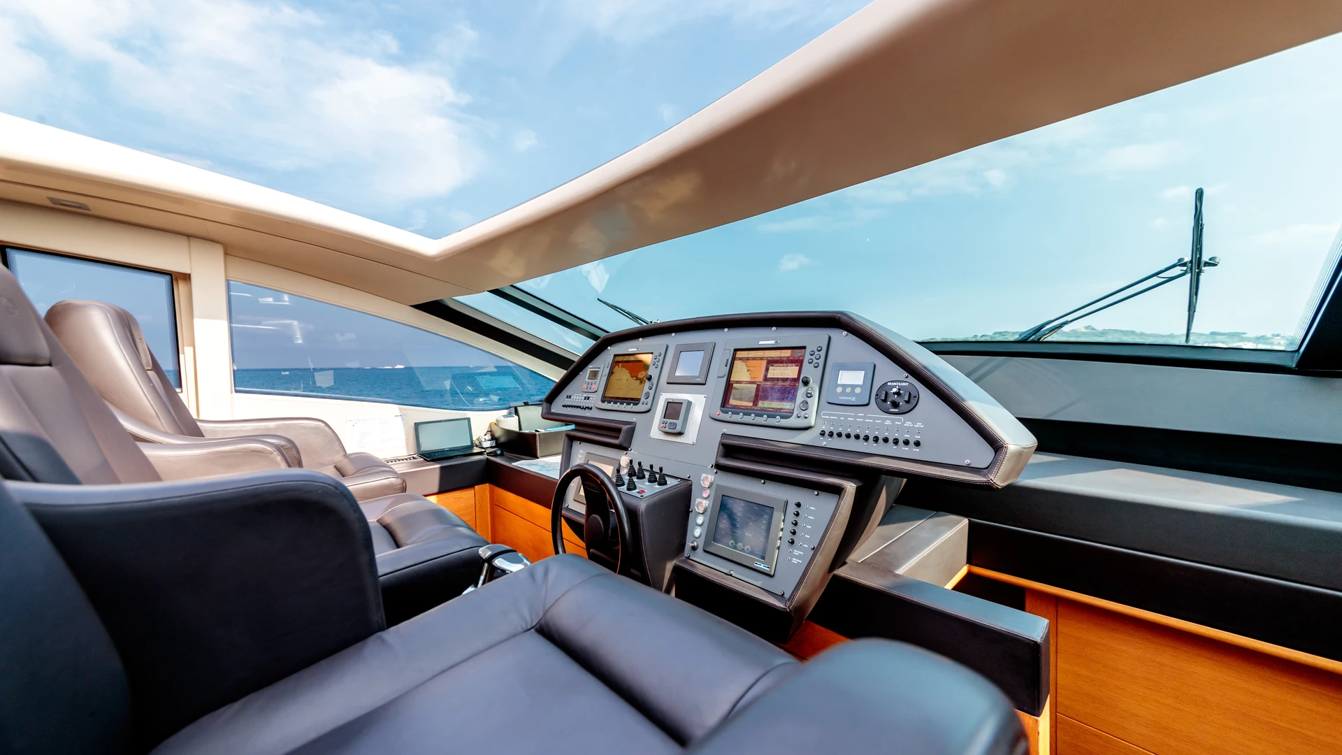 Yacht helm with multiple displays, a steering wheel and upholstered seating