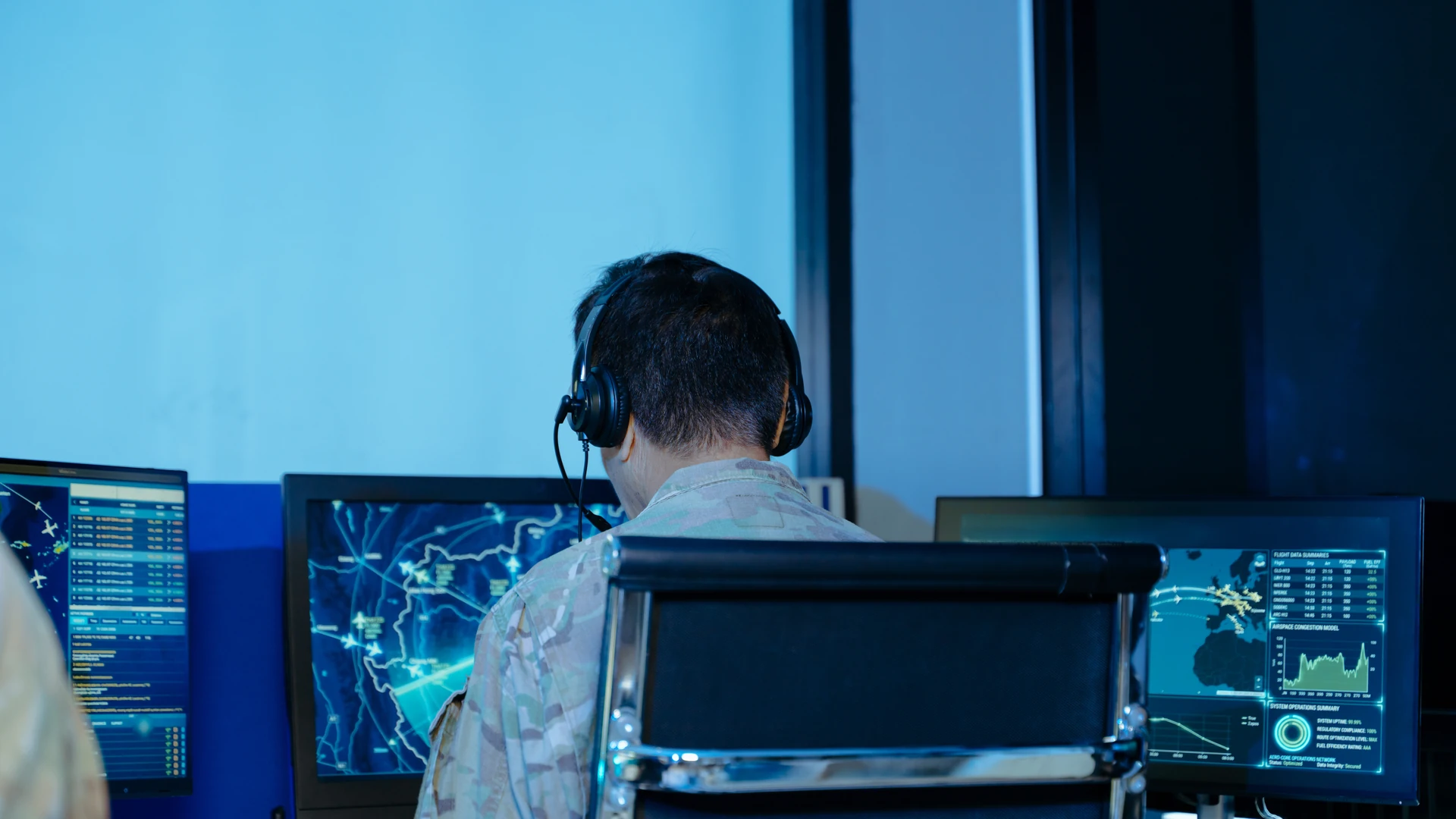 Person wearing a headset at a workstation with multiple map and data displays