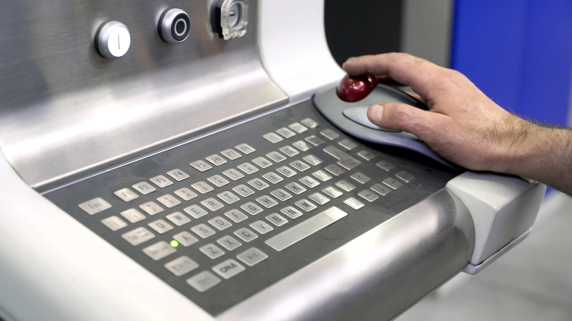 Hand operating a red trackball beside a keyboard mounted in an industrial console