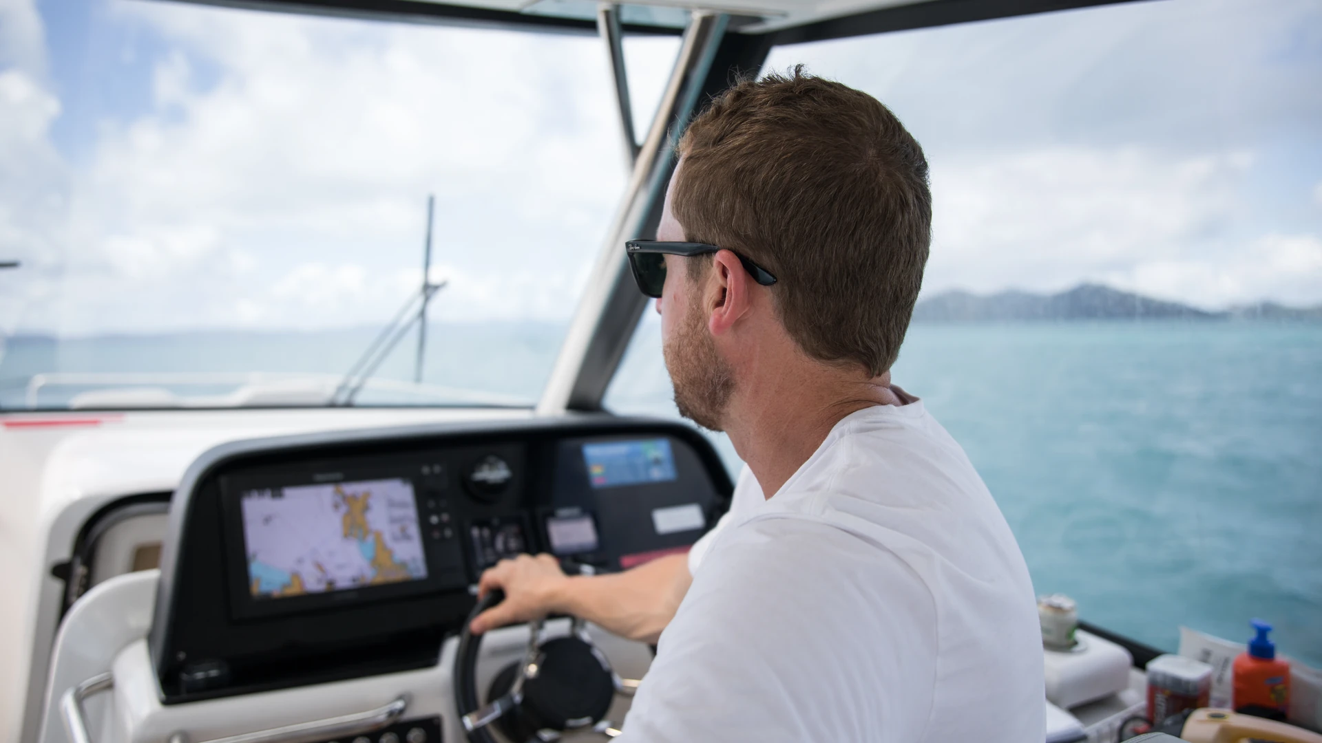 Boater steering beside a helm display showing a nautical chart on open water