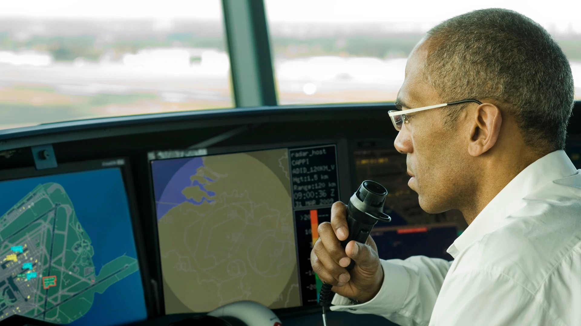 Air traffic controller speaking into a handset beside radar displays in an airport control tower