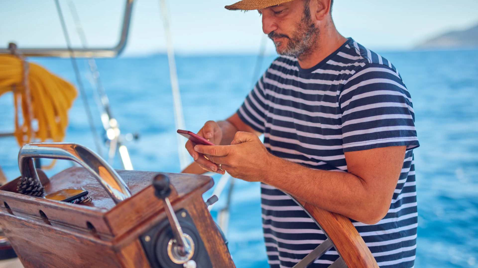 Boater at the wheel of a sailboat using a smartphone on open water