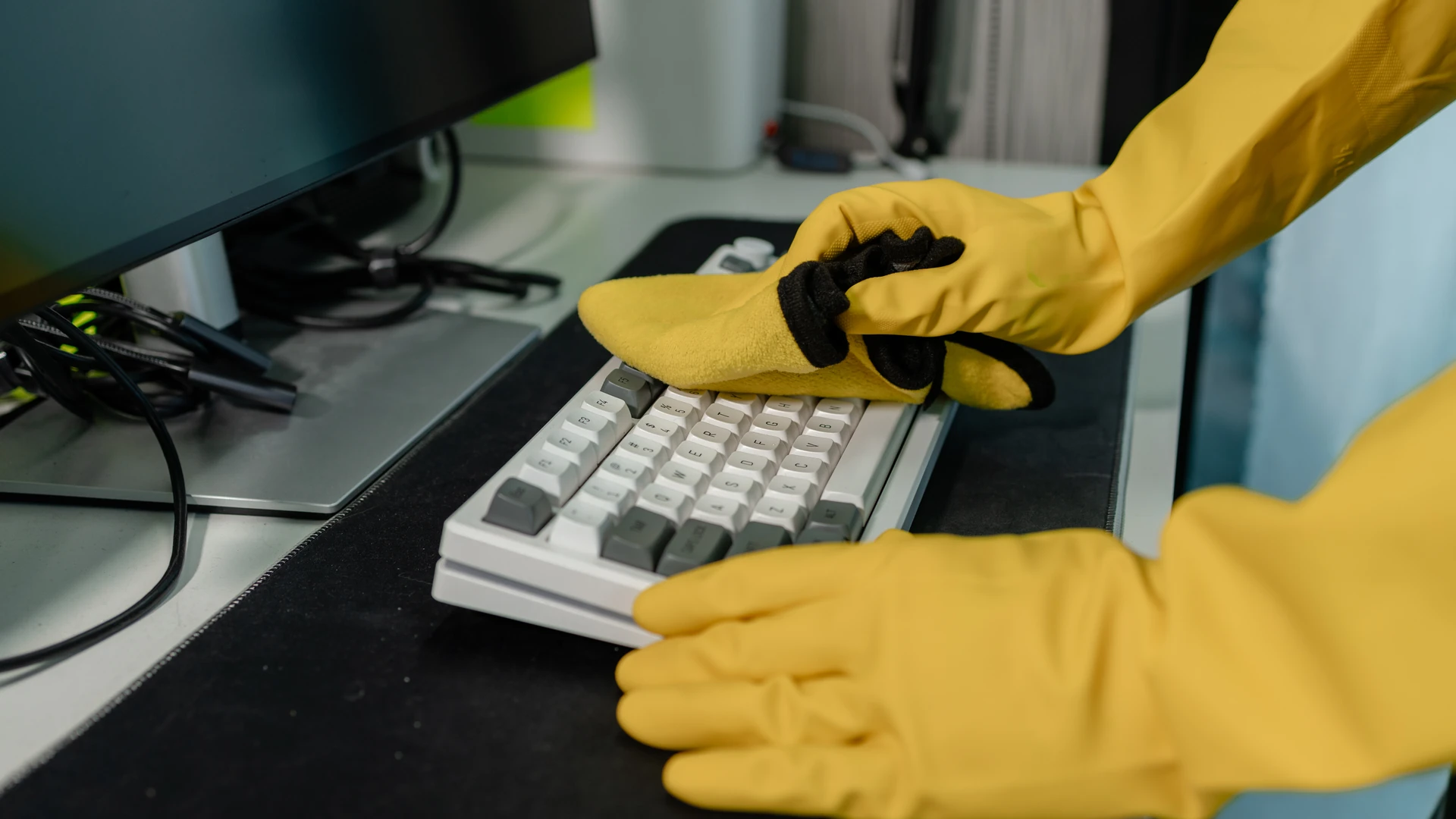 Gloved hand wiping down a keyboard with a cleaning cloth