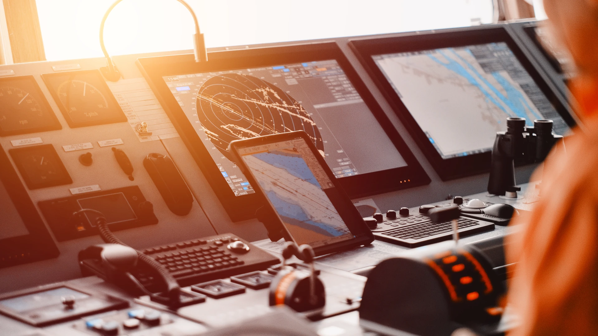 Ship's bridge console with a radar display, an electronic chart display, a tablet showing a chart, keyboards with trackballs and binoculars