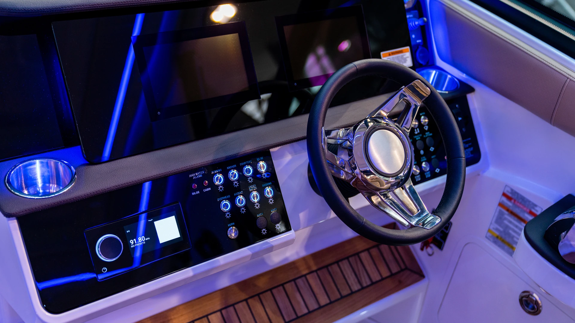 Boat helm with dark glass displays, a polished steering wheel, illuminated switches and blue accent lighting