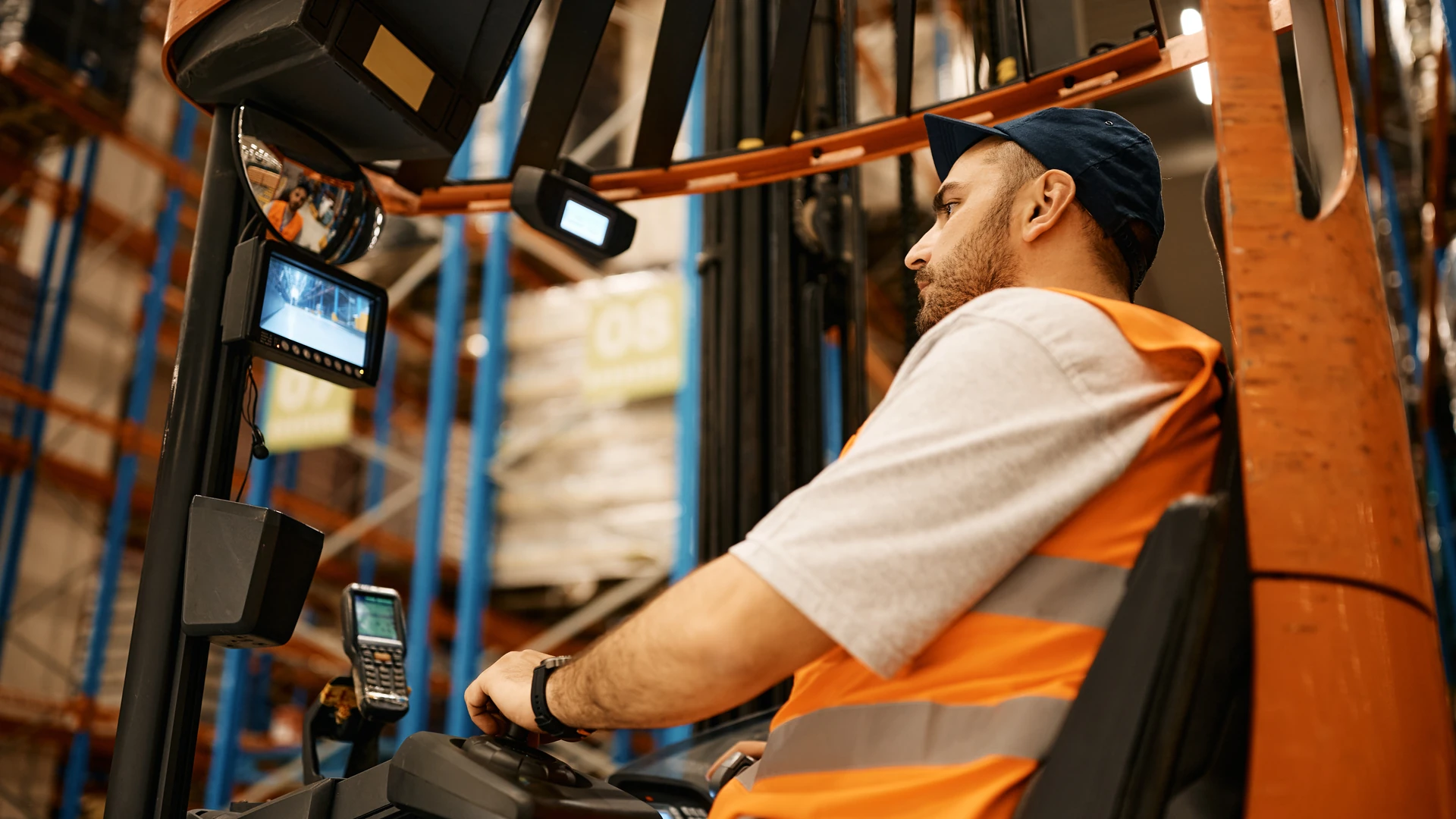 Forklift operator in a warehouse with a camera monitor mounted in the cab