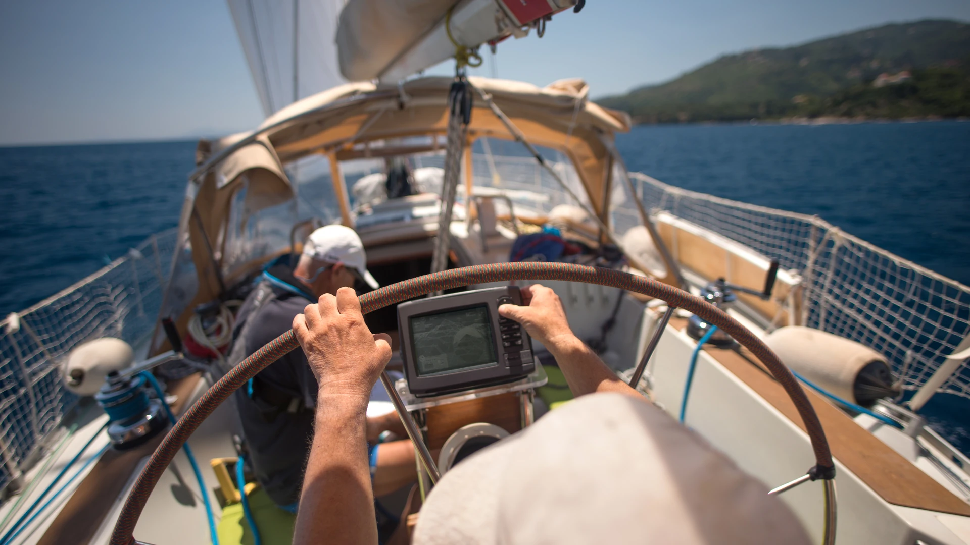 Helmsman's hands on a sailboat wheel around a chartplotter in strong sunlight