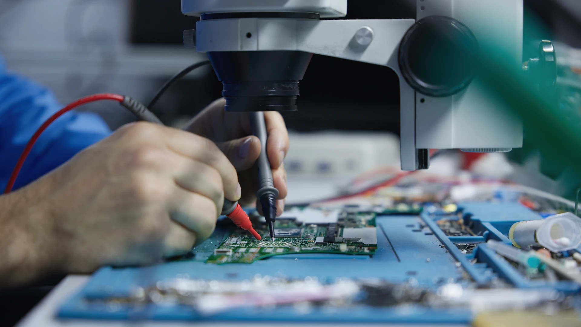 Technician probing a circuit board under a microscope in an electronics test lab