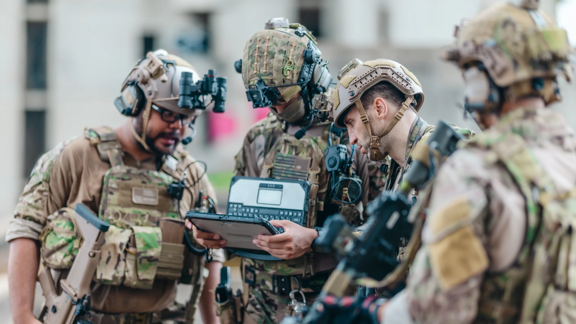 A group in tactical gear looking at a rugged tablet outdoors
